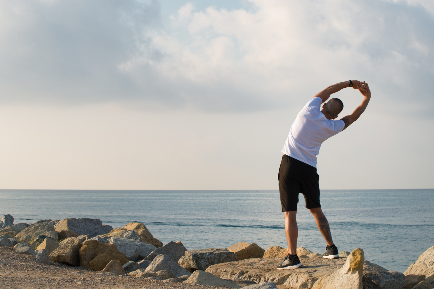 man stretching on the shoreline while exercising mobile medical corporation men's health month